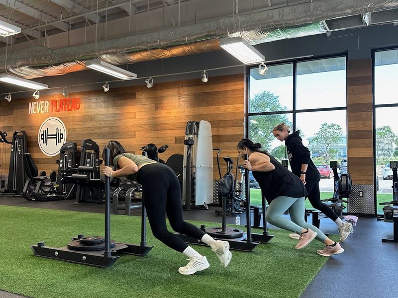 Three clients pushing weighted sleds across the turf lane at Core Progression North Austin