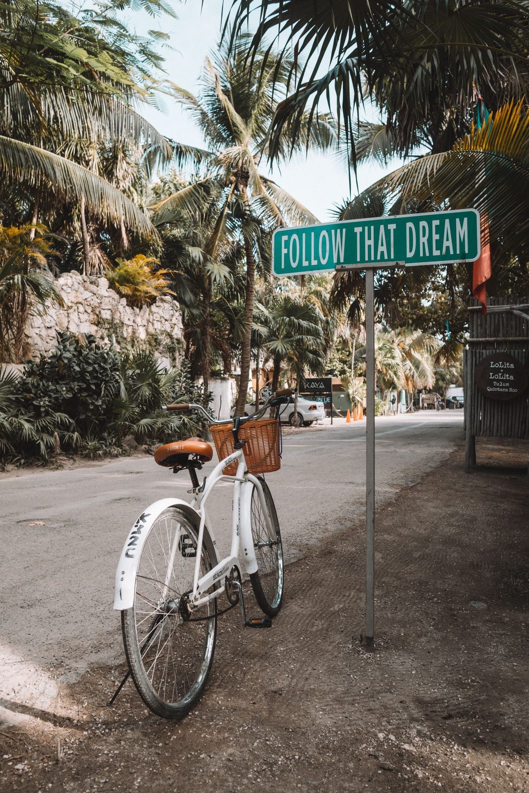 A bicycle parked by the 'Follow That Dream' street sign on Tulum's beach road