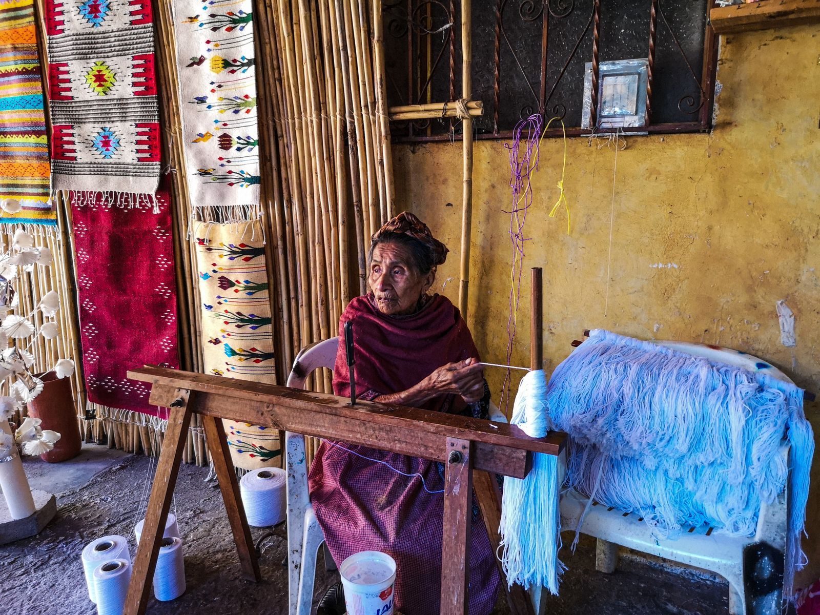 A weaver at her wooden loom in a Teotitlán del Valle workshop, wool rugs hanging on the walls A weaver at her wooden loom in a Teotitlán del Valle workshop, wool rugs hanging on the walls