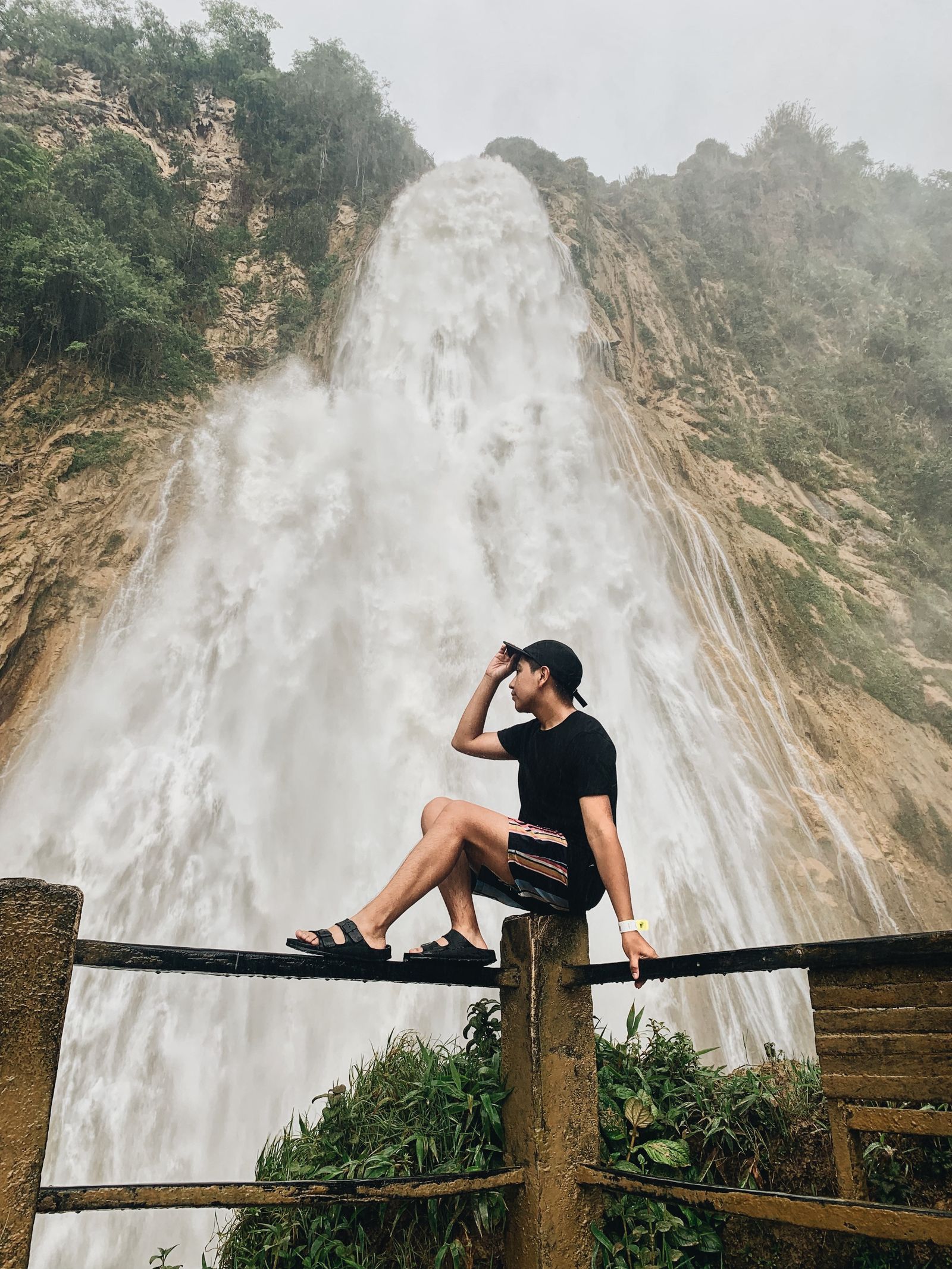 A visitor on the railed viewing platform below a Chiapas waterfall, spray drifting off the fall behind