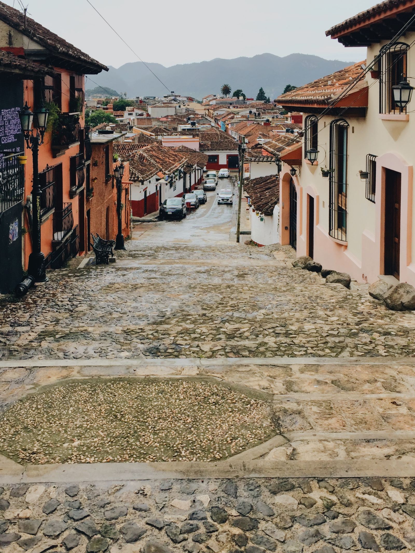 A cobblestone street in San Cristóbal de las Casas with the forested hills that ring the town rising behind the colonial rooftops A cobblestone street in San Cristóbal de las Casas with the forested hills that ring the town rising behind the colonial rooftops