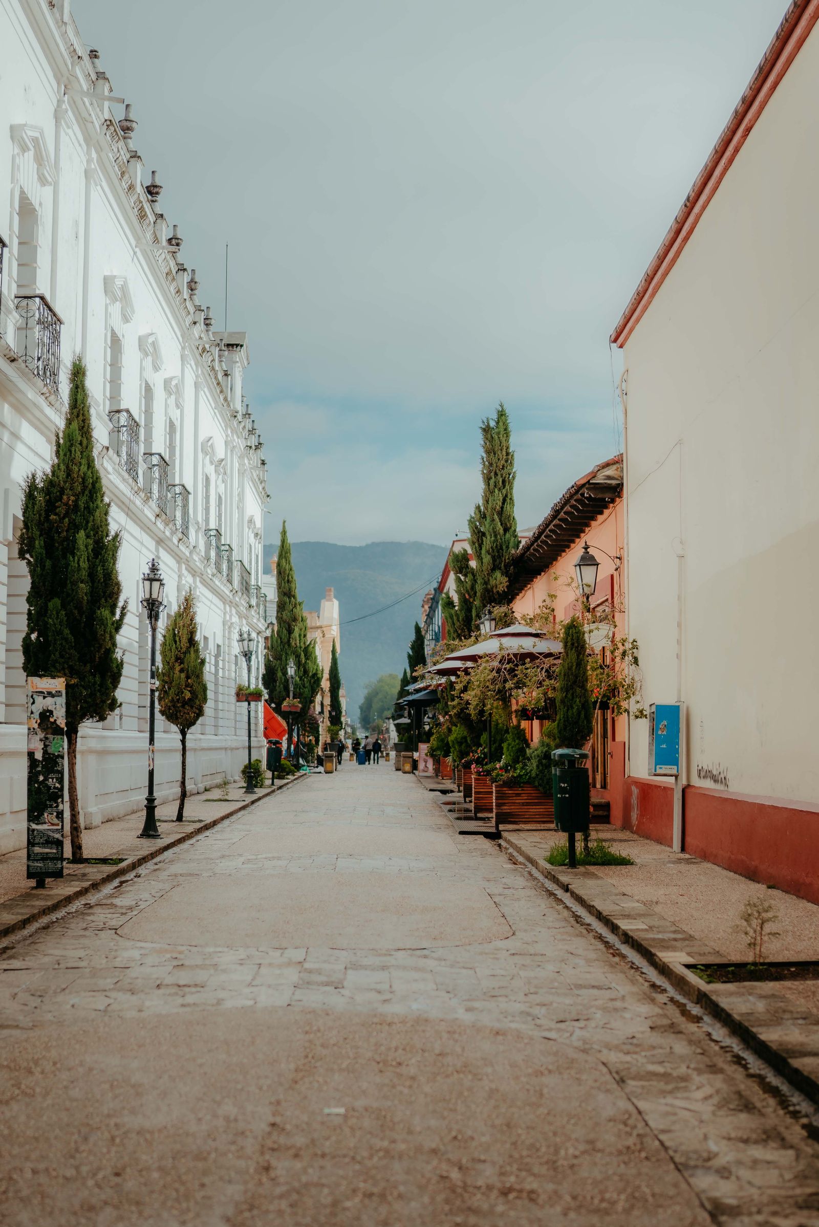 A cobblestone street in San Cristóbal de las Casas on a bright morning, low colonial facades and forested hills behind the town A cobblestone street in San Cristóbal de las Casas on a bright morning, low colonial facades and forested hills behind the town
