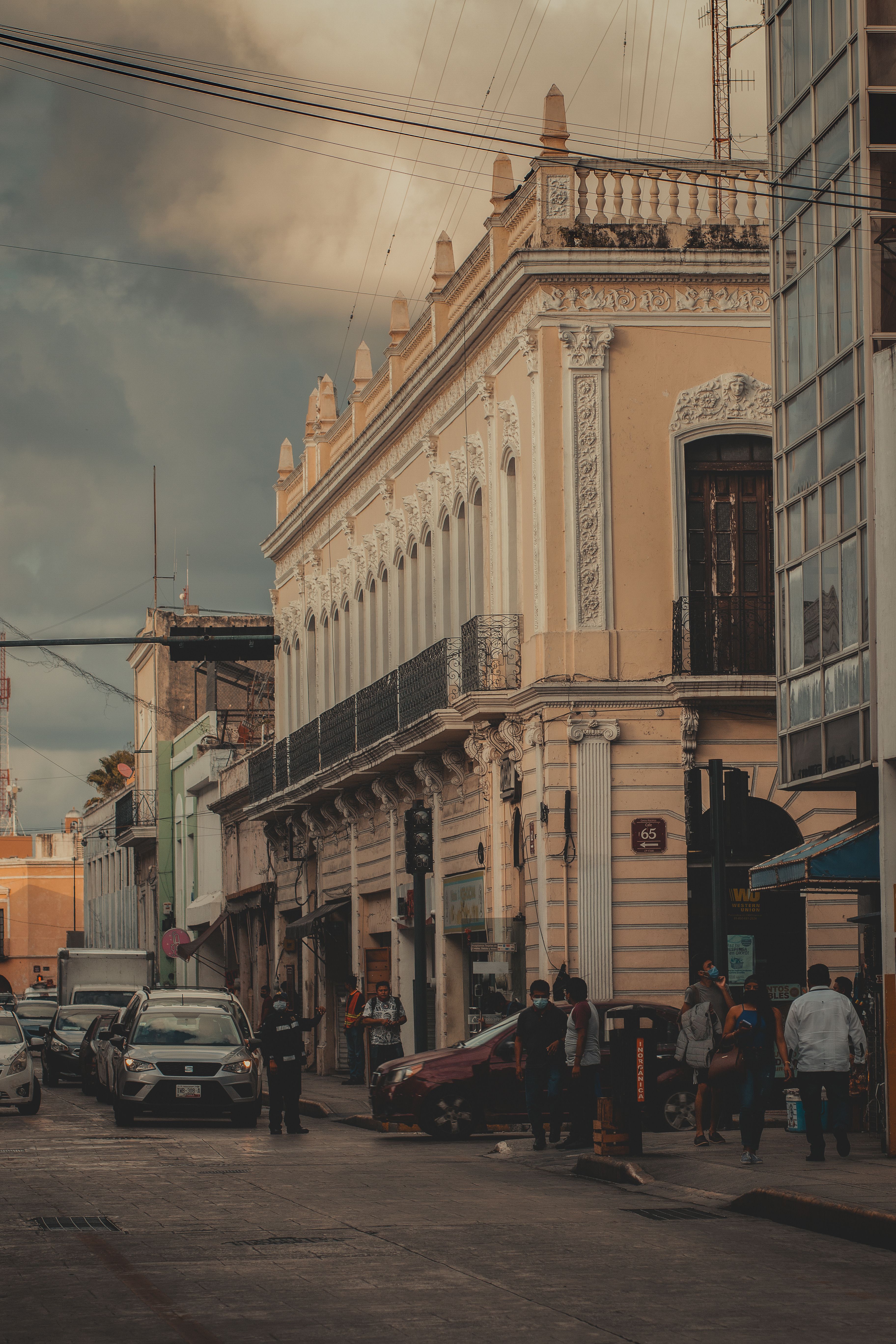 A pastel-colored colonial street in Mérida's Centro at dusk, single-story houses in yellow and blue, a couple of people walking.