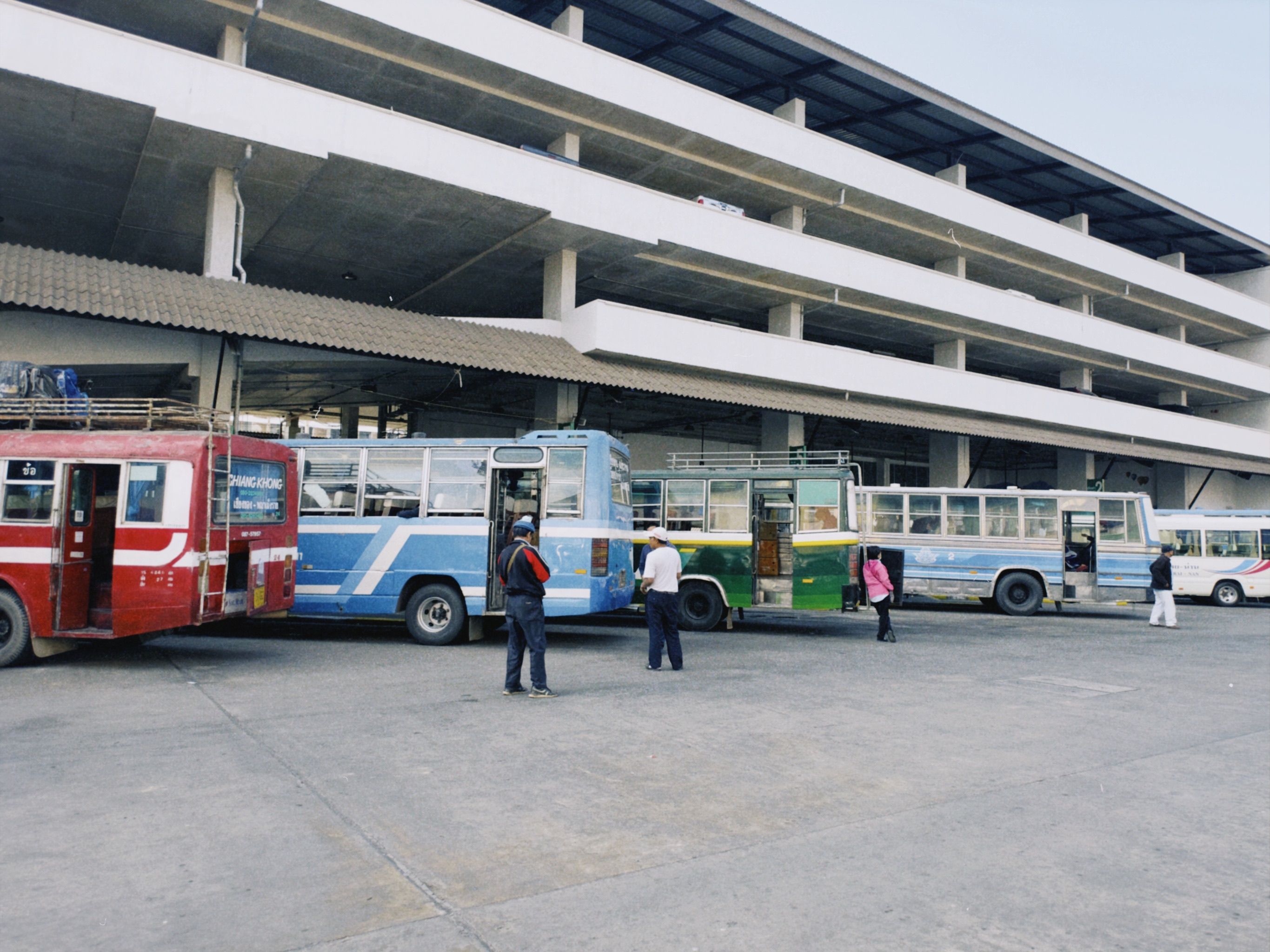 A first-class ADO bus pulling into a small Yucatán town station, palms and a low ochre building behind it