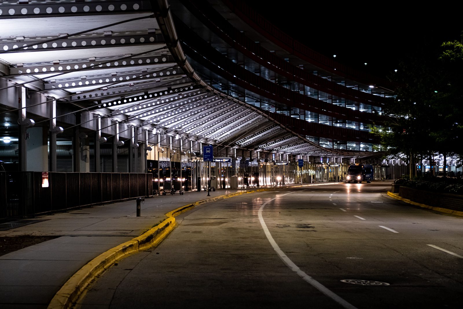 The exterior arrivals curb of a Cancún airport terminal, a row of ADO buses and taxis waiting, palm trees and tropical heat haze visible The exterior arrivals curb of a Cancún airport terminal, a row of ADO buses and taxis waiting, palm trees and tropical heat haze visible