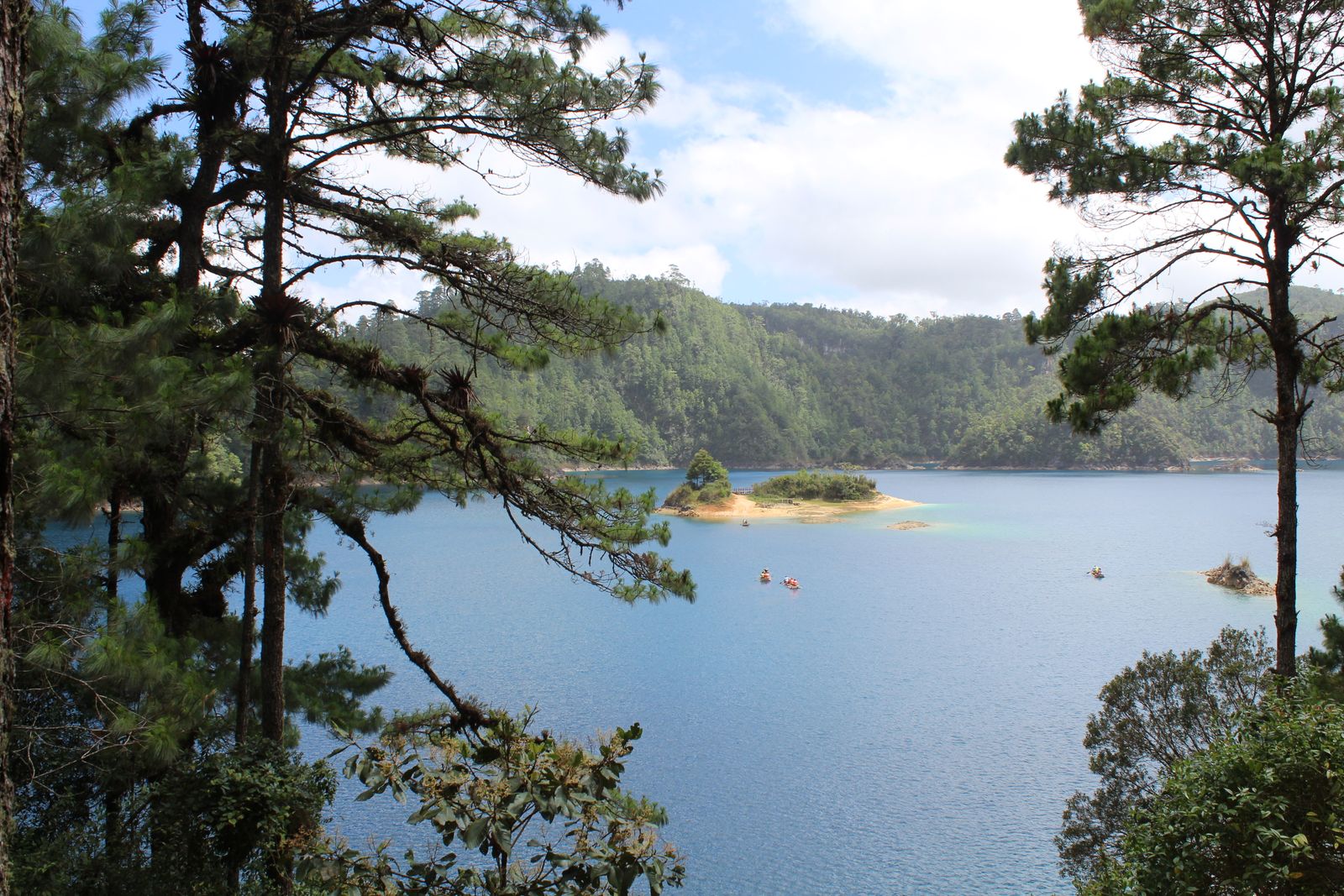A Lagos de Montebello lake ringed by pine forest under a cloudy highland sky, the water deep teal and still