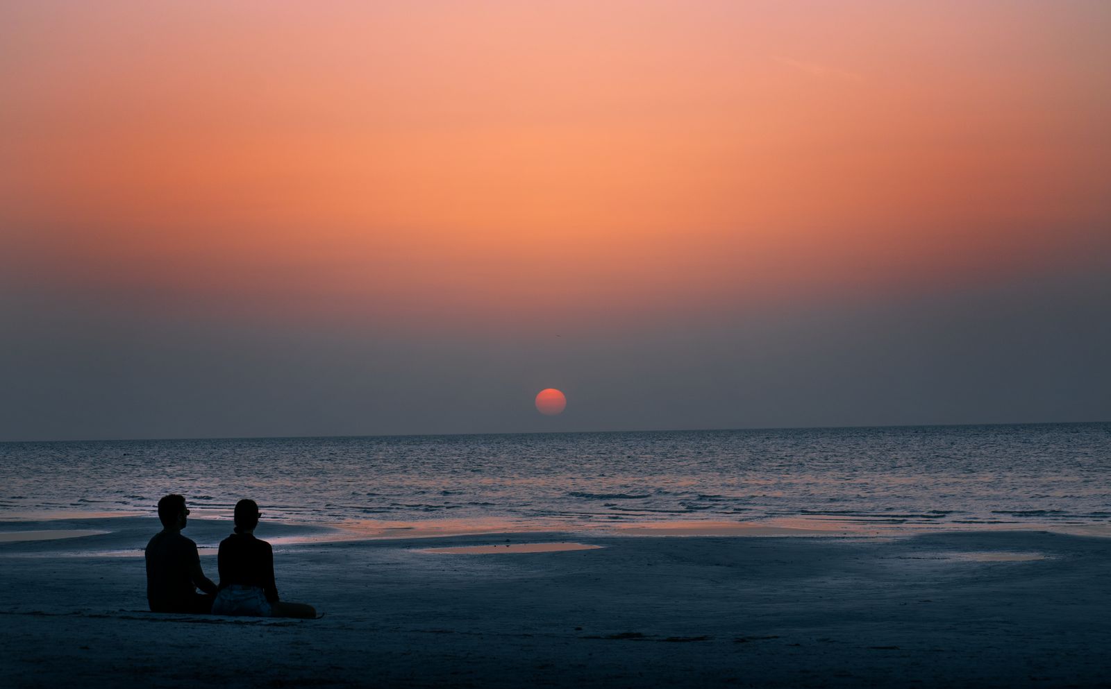 A couple sitting on the beach in Holbox watching the sun set over the water