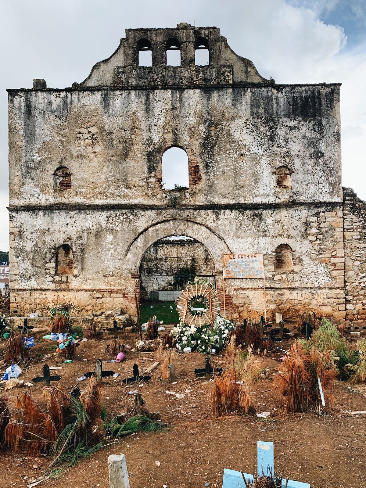 The roofless ruin of the old San Sebasti&aacute;n church in Chamula's cemetery, with grave mounds and pine-needle offerings in front