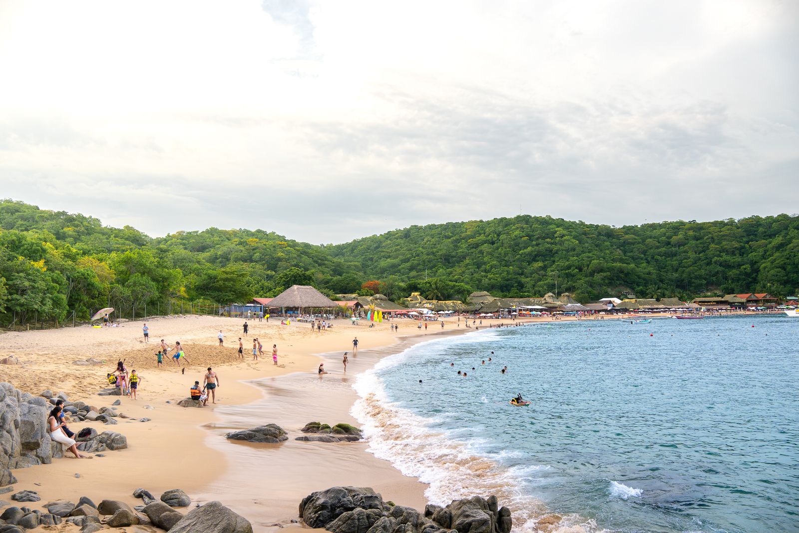 A busy sandy beach on one of the bays of Huatulco, Oaxaca, framed by forested hills