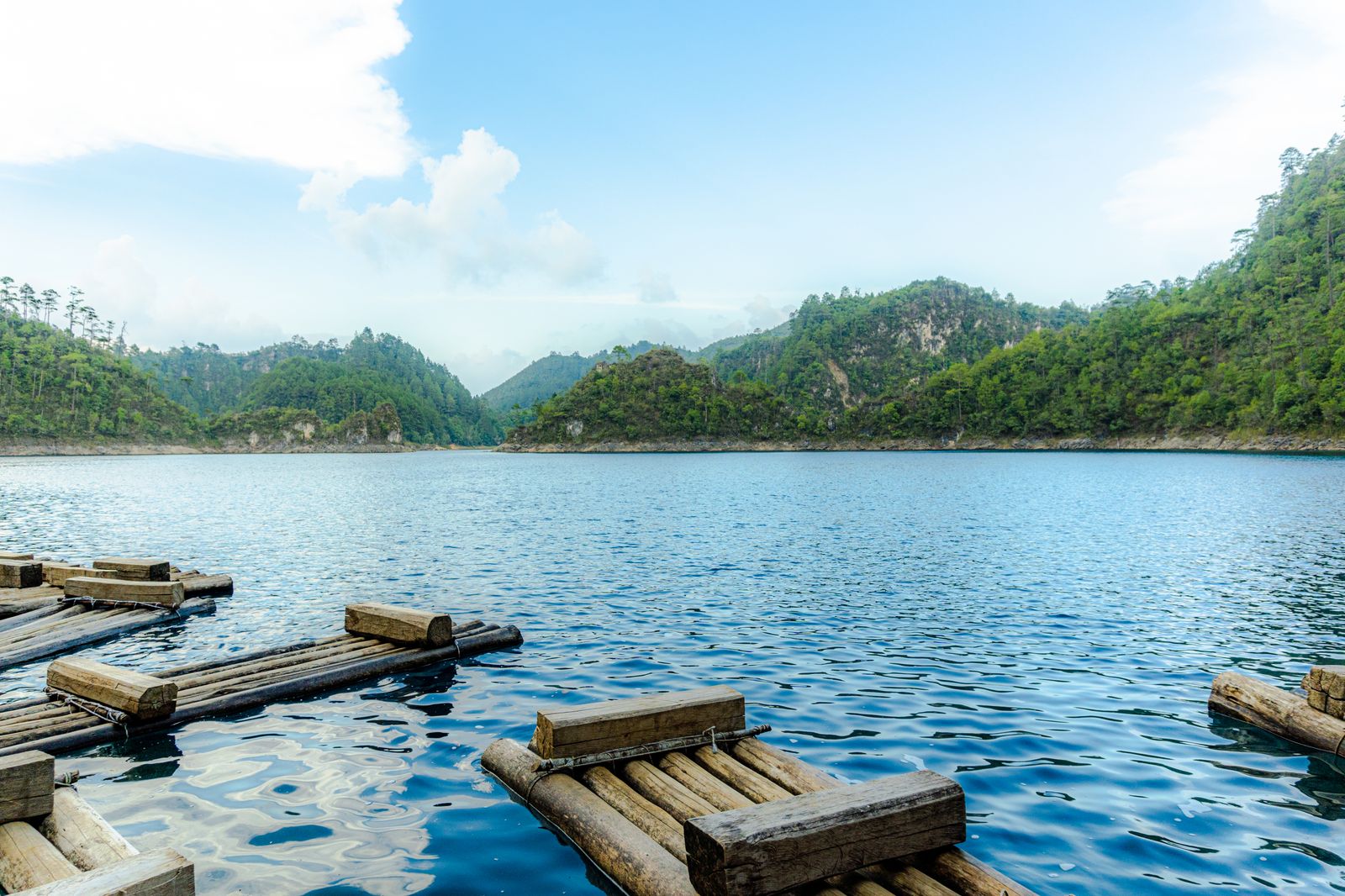 Wooden balsa rafts tied up on a turquoise Montebello lake, forested hills behind