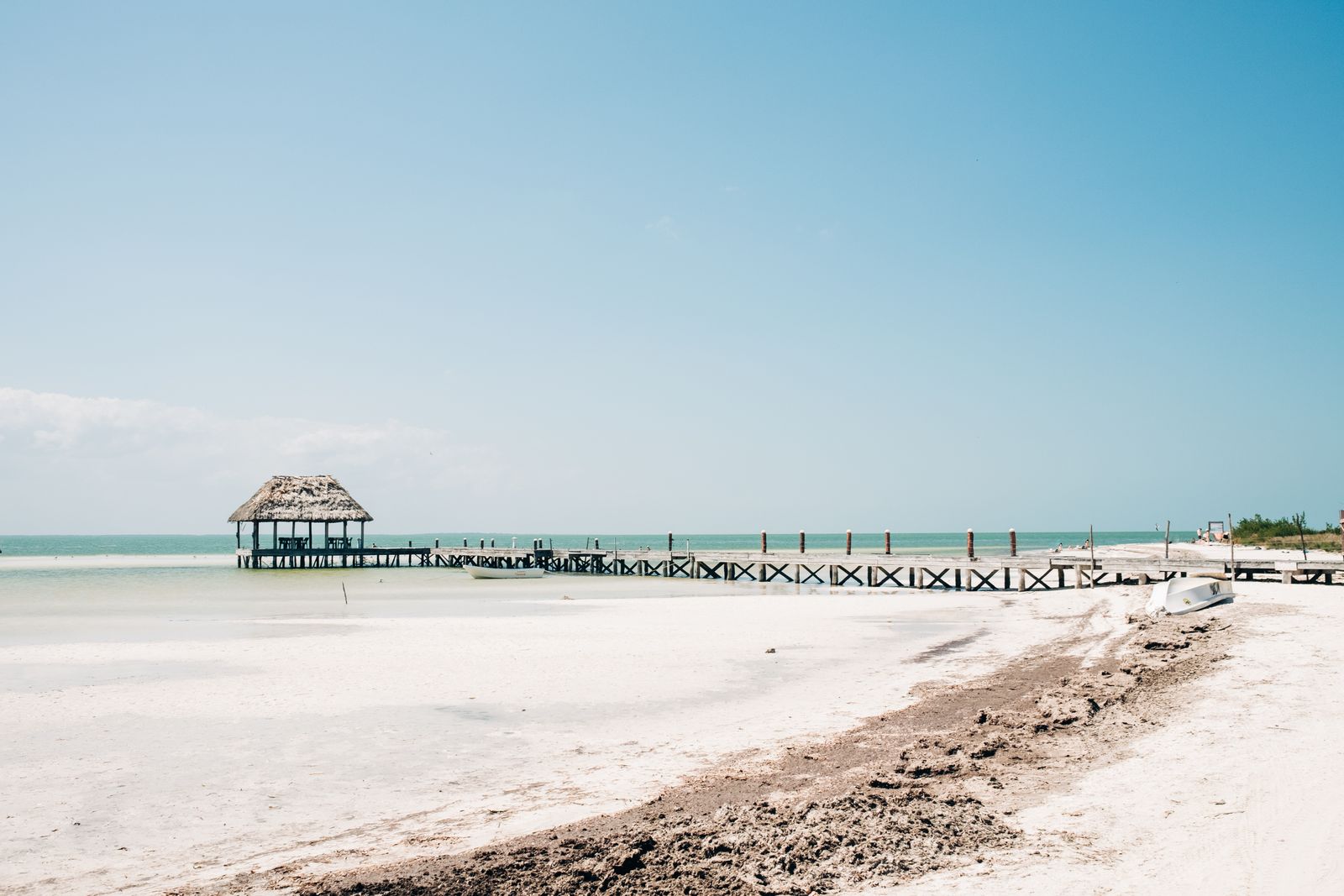 A long wooden pier with a palapa at the end off a white-sand beach on Holbox