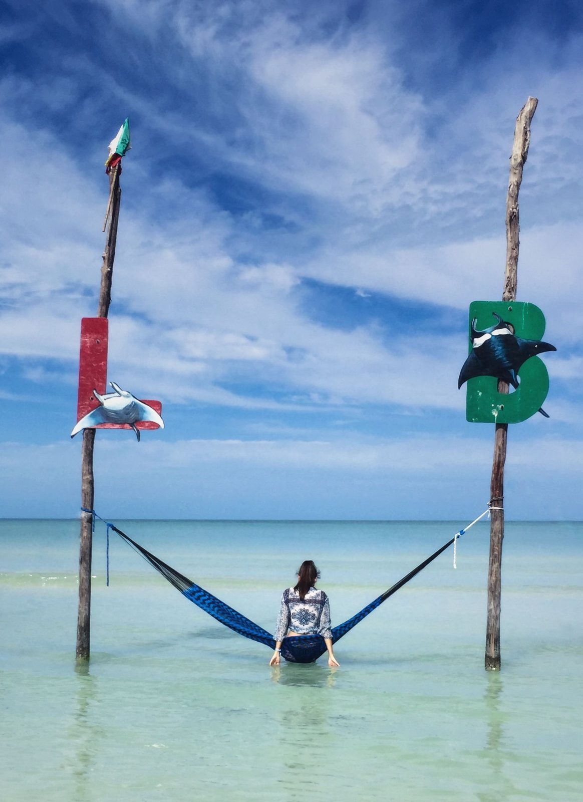 A woman in a hammock strung between two posts in the shallow water off Holbox