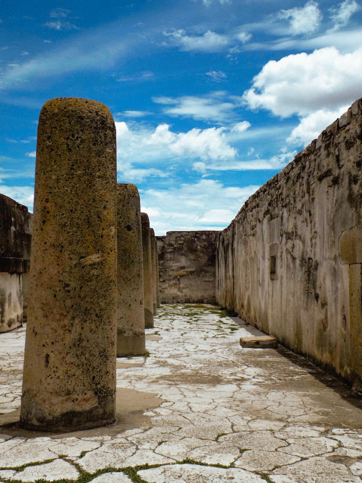 The Hall of Columns at Mitla, a row of thick monolithic stone columns inside a long roofless stone hall under a blue sky