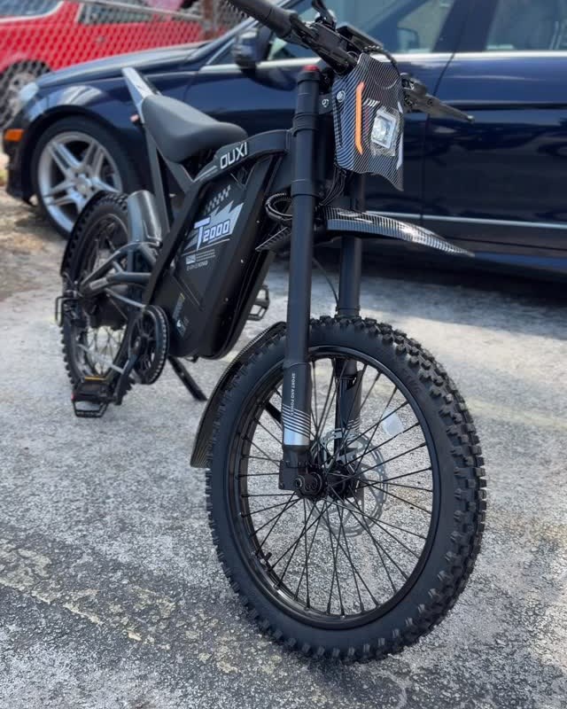 A black electric dirt bike on the lot beside parked cars.