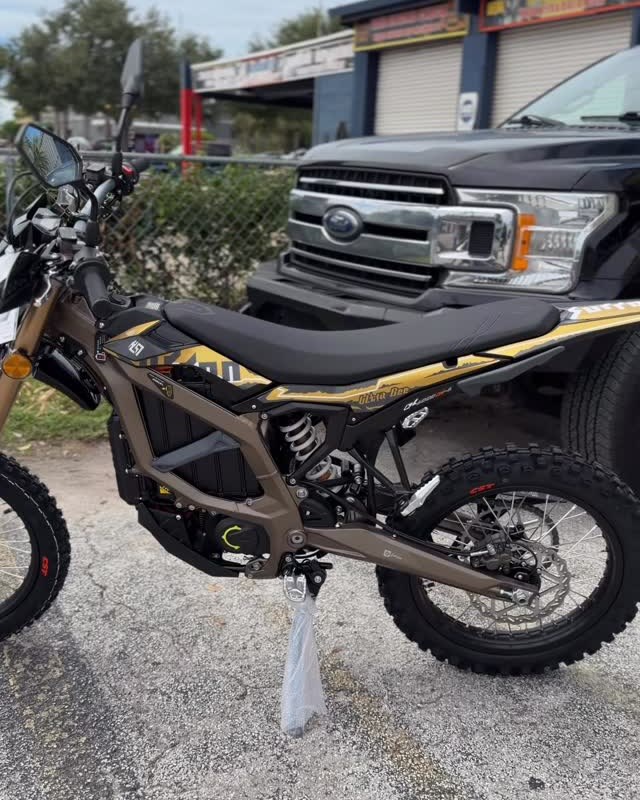 A bronze and black electric dirt bike on its stand on the lot.