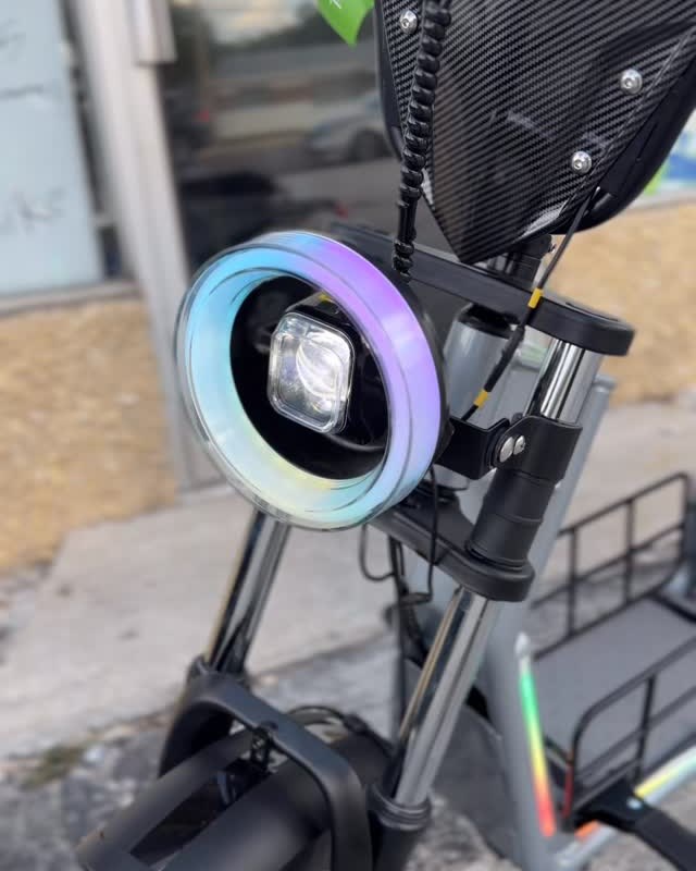 Close on an ebike's front, a ring headlight glowing under a carbon fairing.