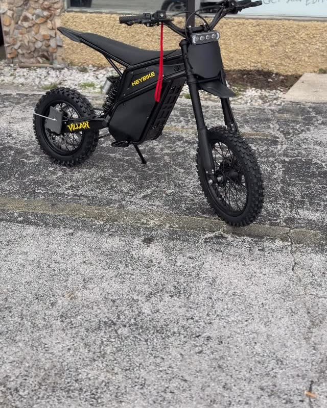 A black moto-style ebike with a red tag on the lot by the shop.