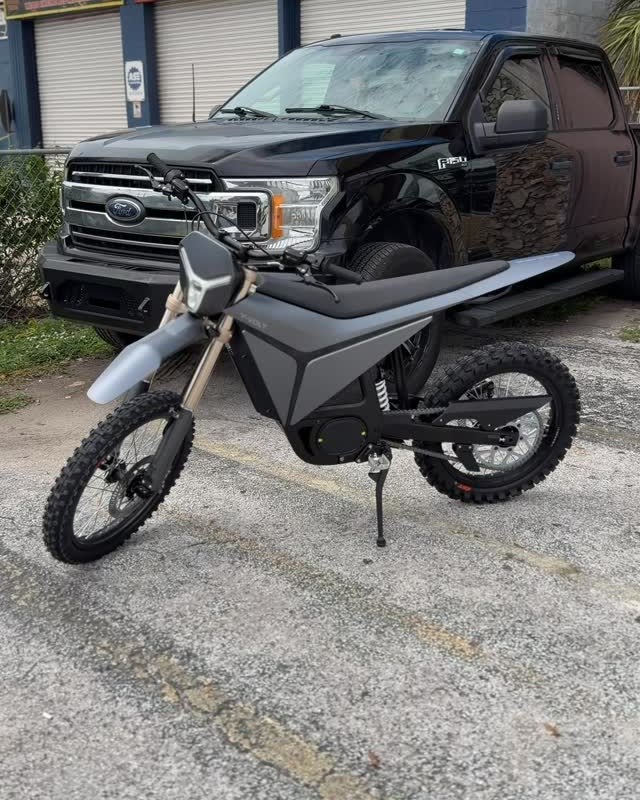 A black electric dirt bike on its stand on the lot.