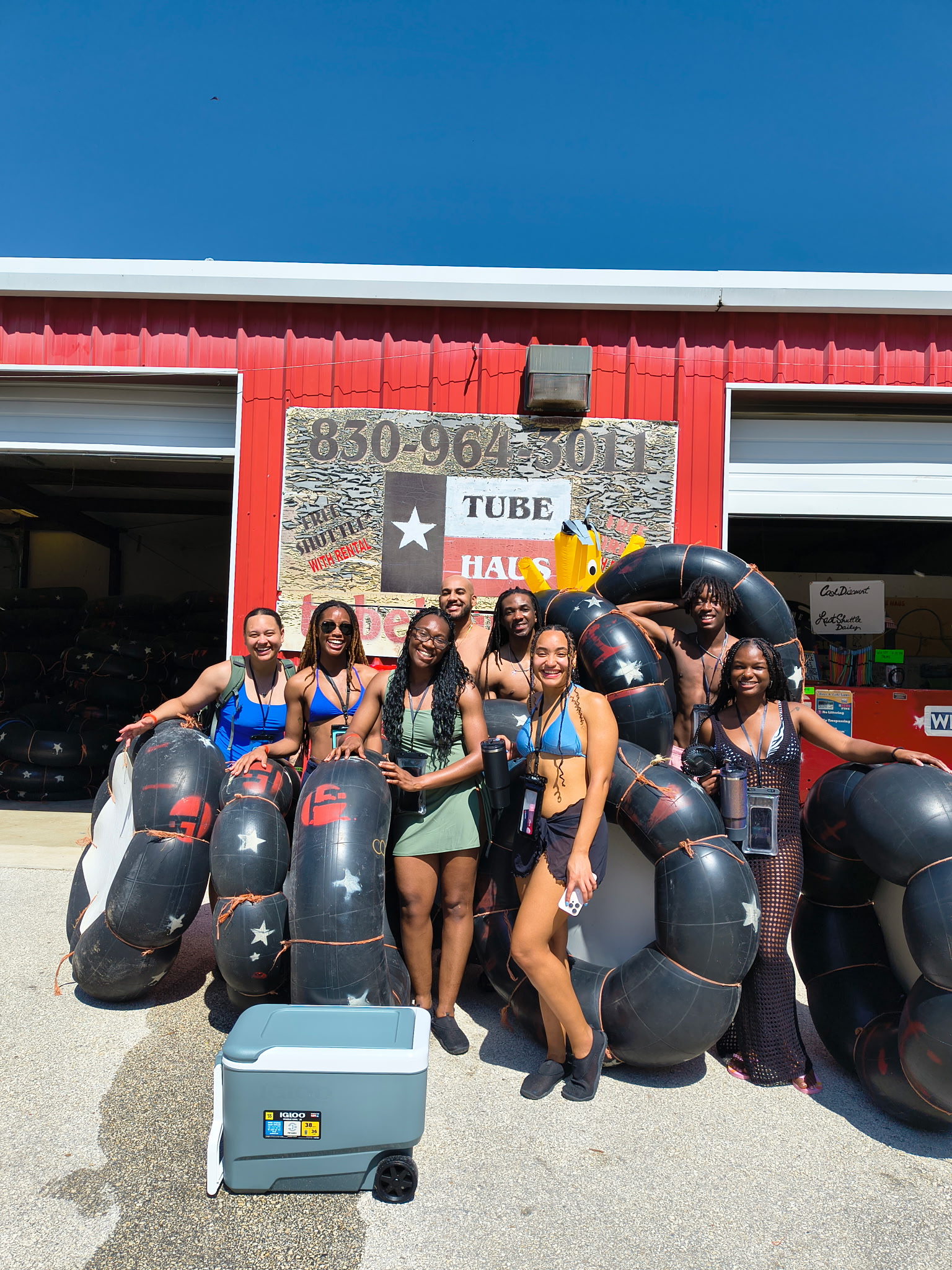 Group of friends with river tubes and a cooler outside Tube Haus before a BYOB tubing trip near Canyon Lake, Texas.