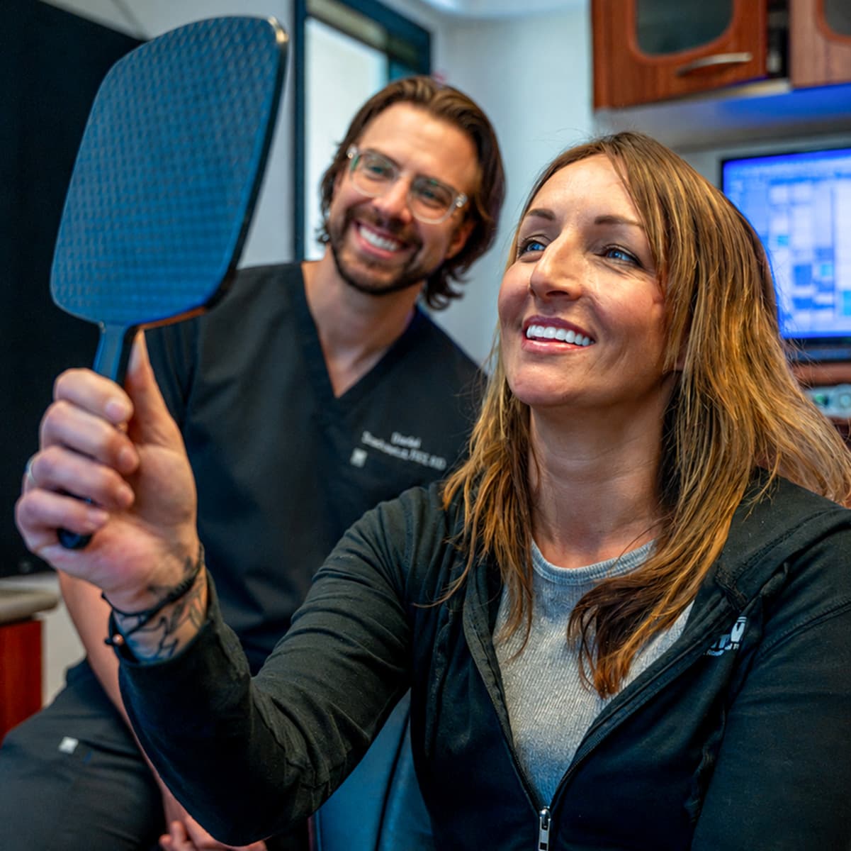 A patient seeing her new smile in a hand mirror with Dr. Daniel Stackowicz beside her