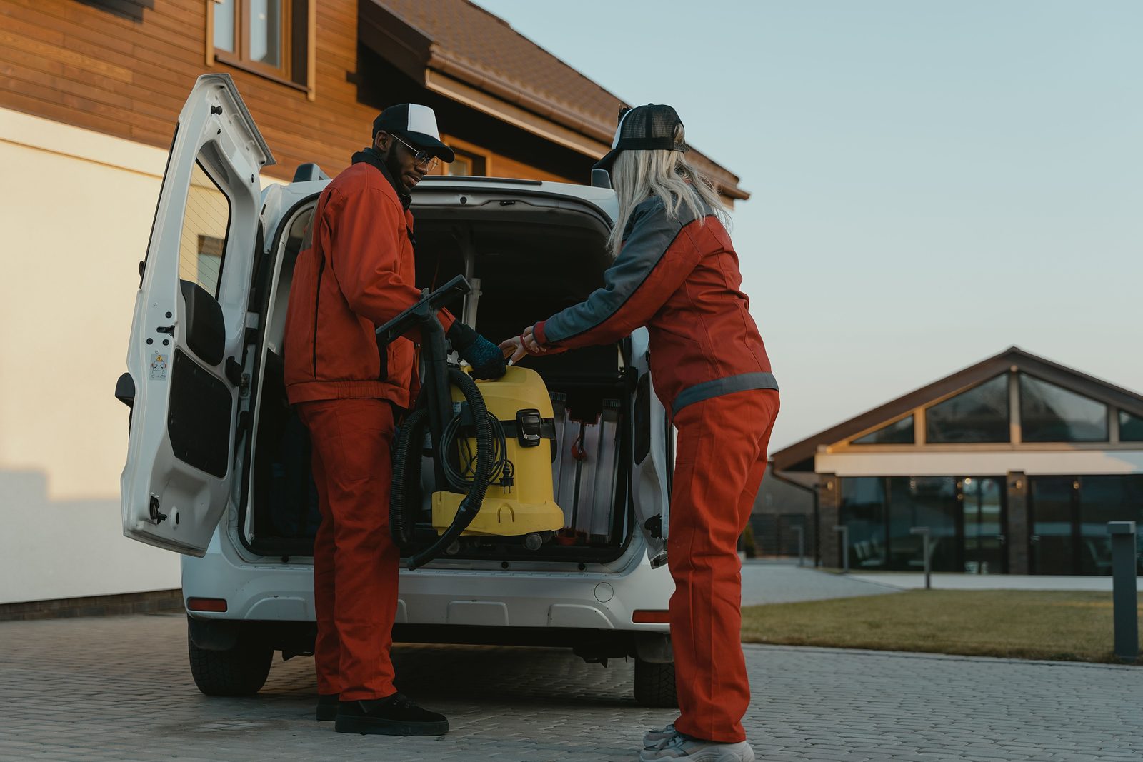 Two cleaning workers unloading equipment from a service van