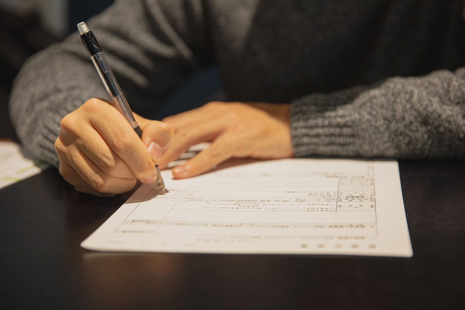 Hands filling in a paper form with a pen at a table
