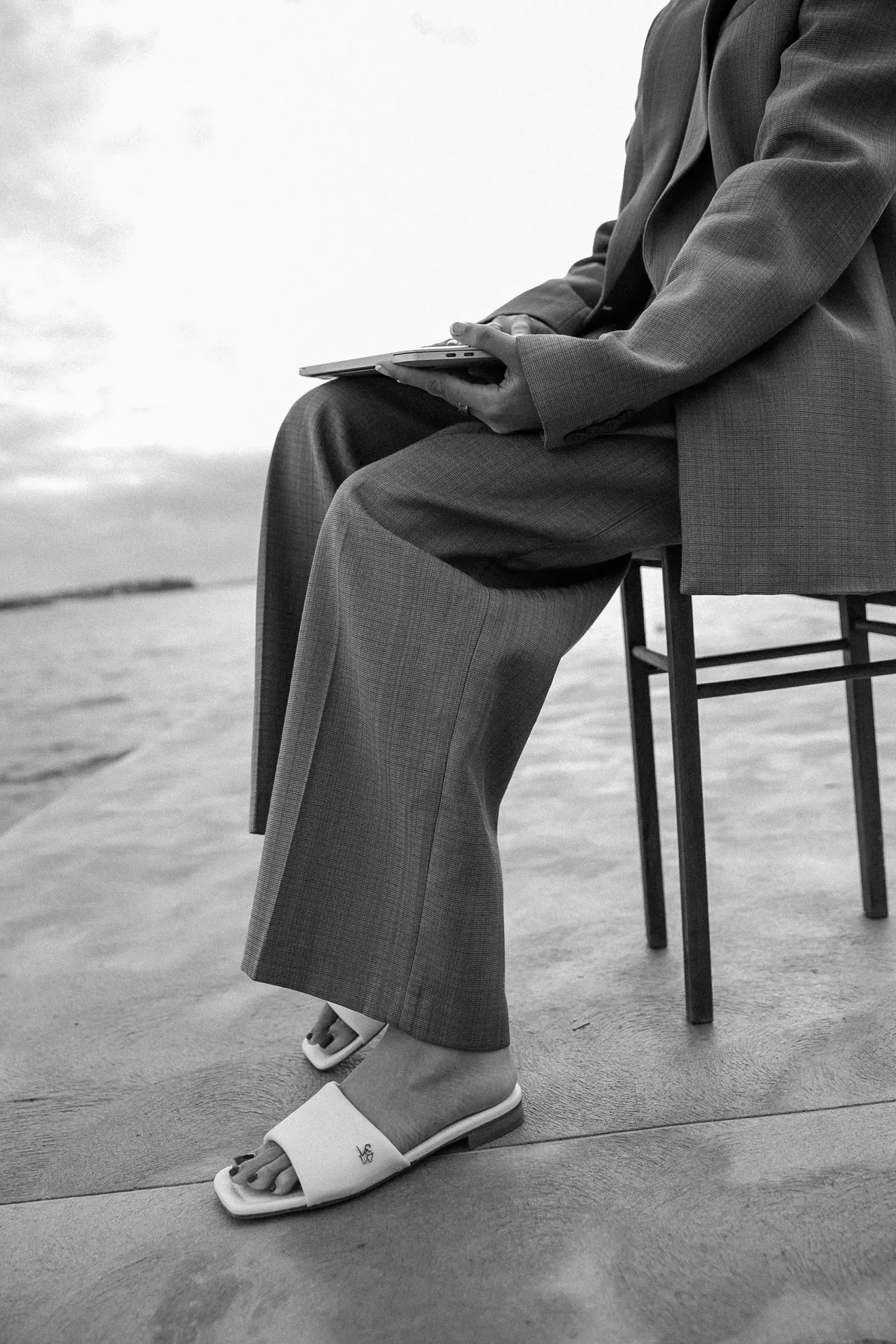 Saddy seated on a chair by the water, in a suit, a laptop on her knee