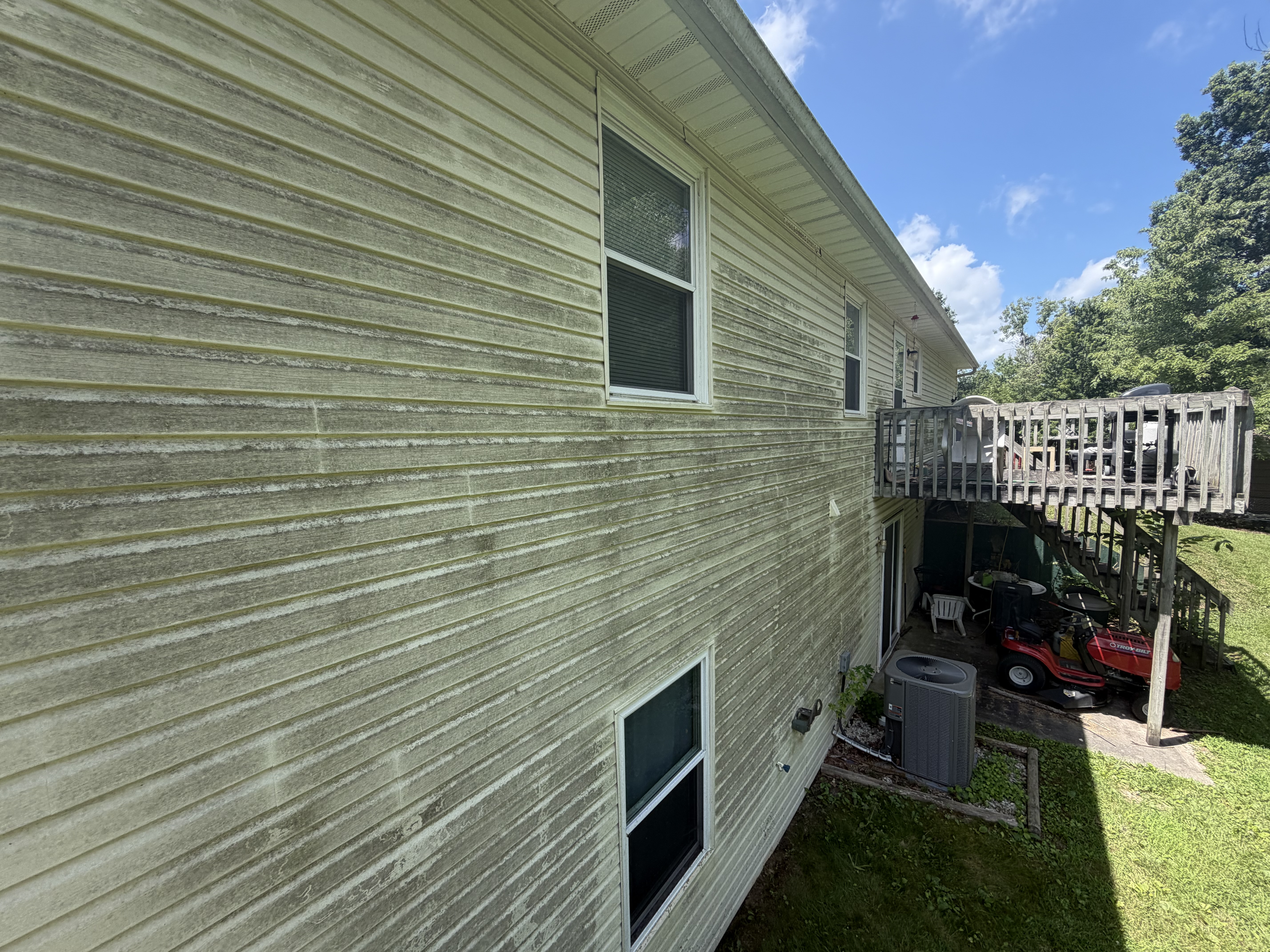 A two-story home with siding and a deck, set among mature trees.