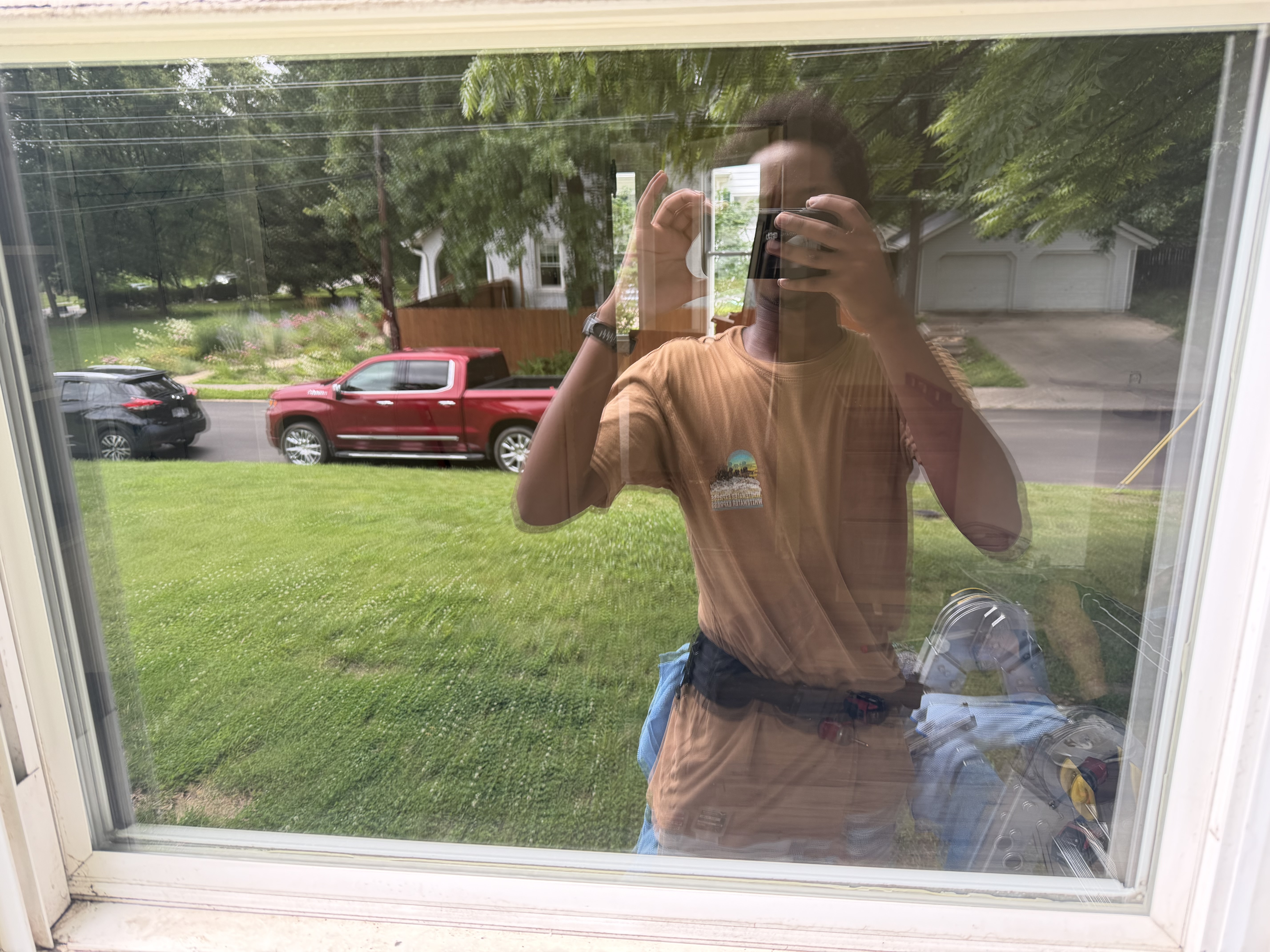 A window cleaner standing beside a work truck loaded with ladders and cleaning equipment in a sunny driveway.