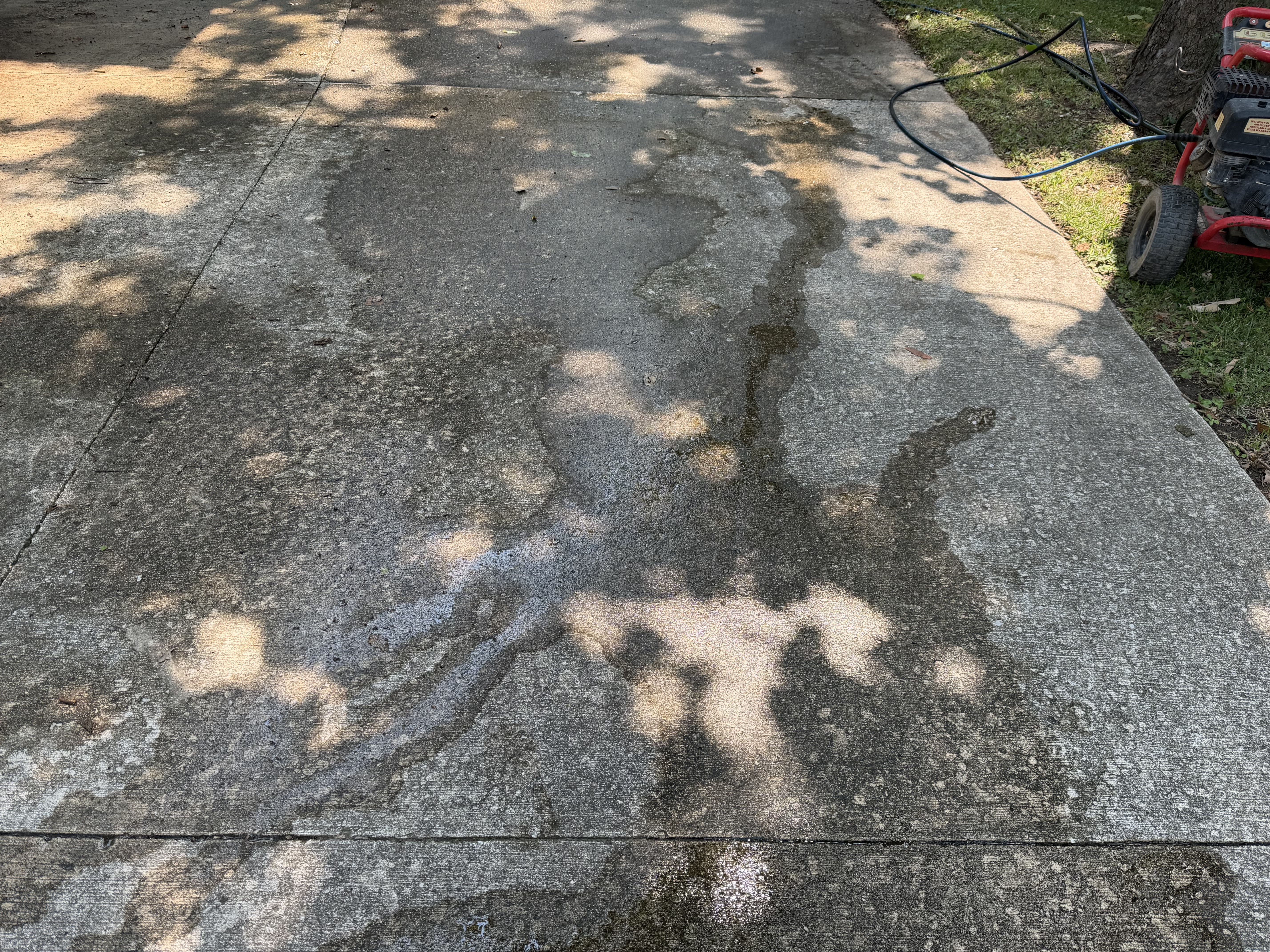 A concrete surface being pressure washed, with the pressure washer visible at the edge.