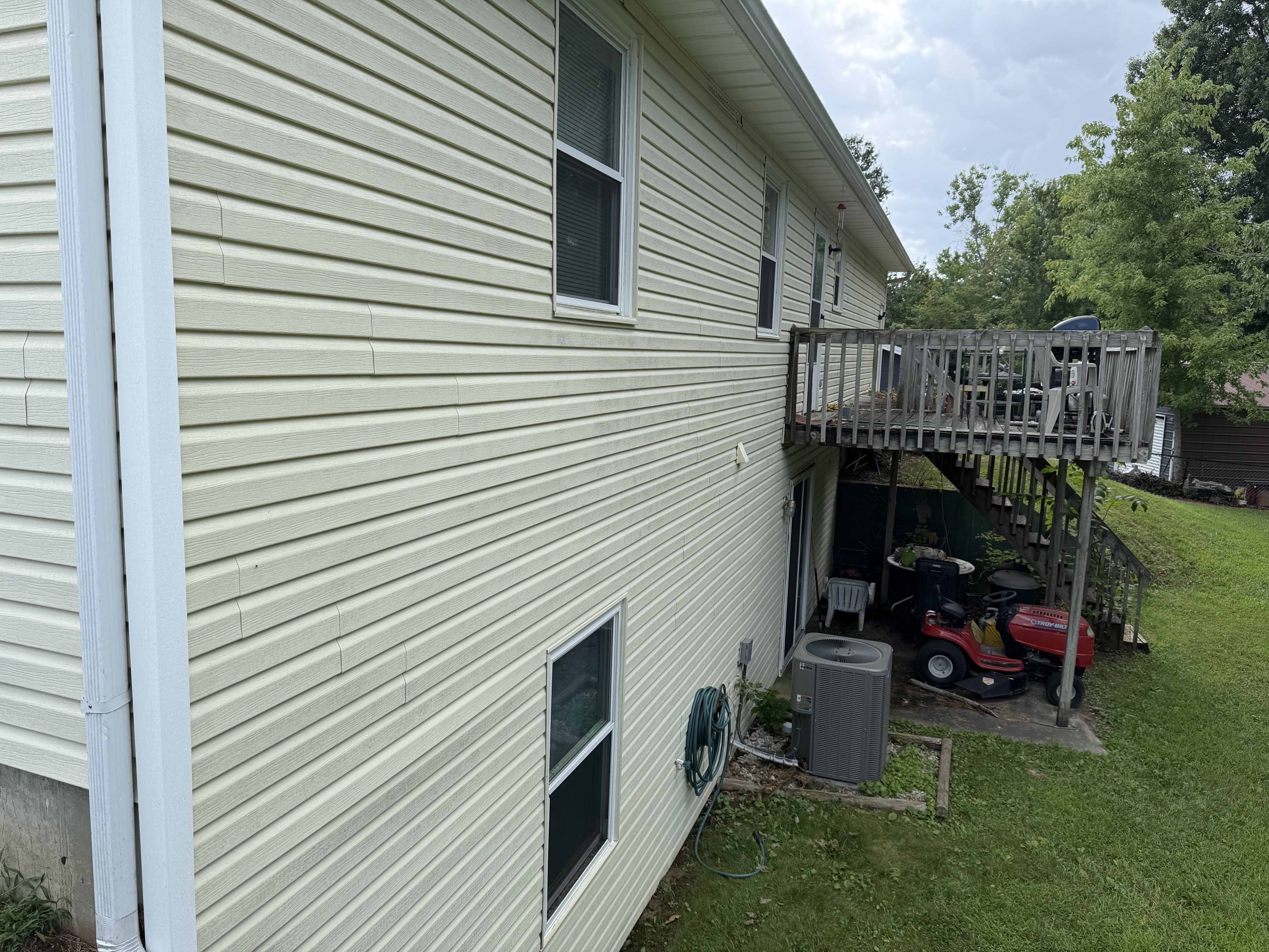 The side of a house with light siding, a white downspout, windows, and a deck.