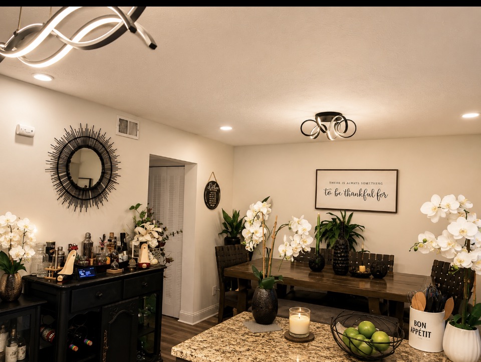 Dining and entertaining space with wood dining table, black furnishings, white orchids, greenery, and decorative accents.