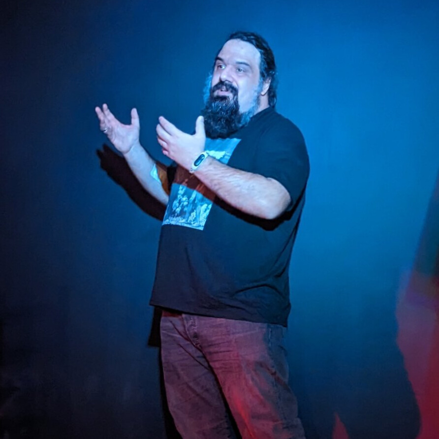 Dr. Orestis Vasilakis On Stage Giving a Talk With Hands Extended in an inspirational manner