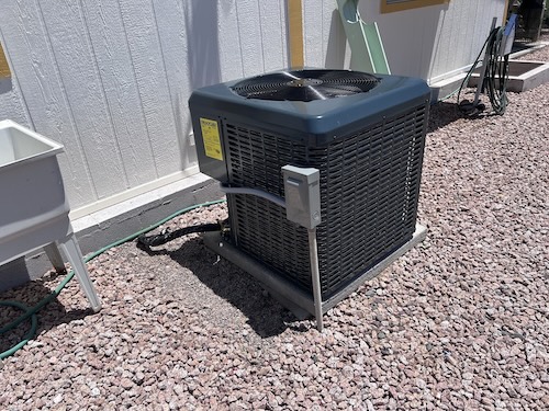 Outdoor AC condenser unit on a concrete pad in a gravel yard at an Apache Junction, AZ home serviced by Rush HVAC Services