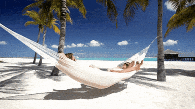 Person relaxing in a white hammock between palm trees on a sunny tropical beach with turquoise ocean in the background. Person relaxing in a white hammock between palm trees on a sunny tropical beach with turquoise ocean in the background.