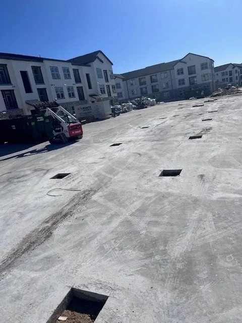 A cleared and graded residential lot in San Antonio, Texas, with old concrete removed and bare soil leveled in preparation for new construction. A demolition contractor's equipment sits at the edge of the site after completing site preparation work.