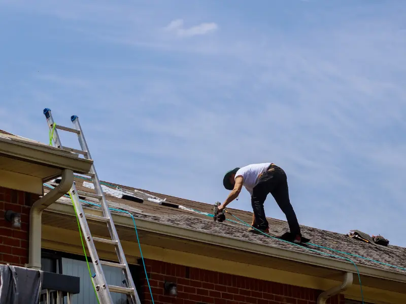 Local roofing contractor nailing down new shingles along the roofline.