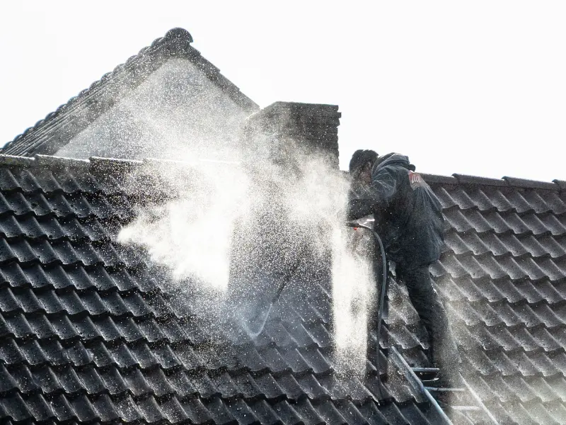 Worker pressure washing tile roof to remove dirt and debris.