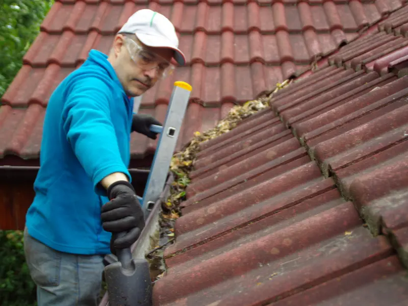 Gutter cleaning worker clearing debris from a tiled roof gutter.