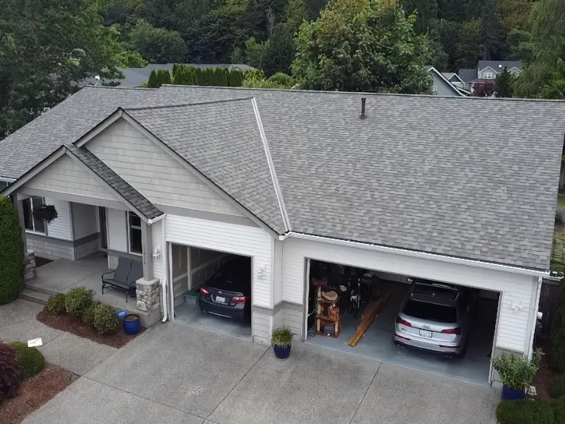 Aerial view of a house with a new asphalt shingle roof installed by a roofing contractor.