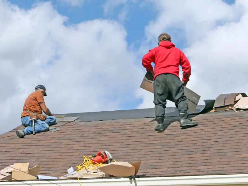 Two roofers replacing old shingles during a roof replacement project.