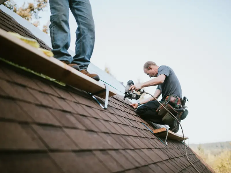 Roofer using a nail gun to install new shingles during roof replacement.