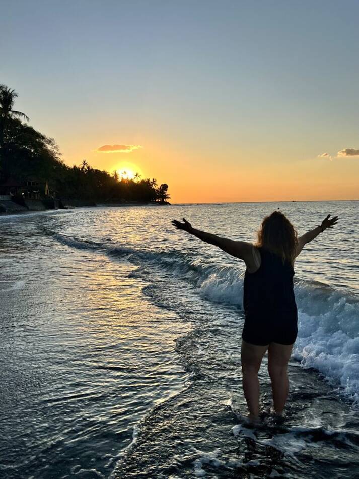 A woman standing in the sea at sunset, arms open