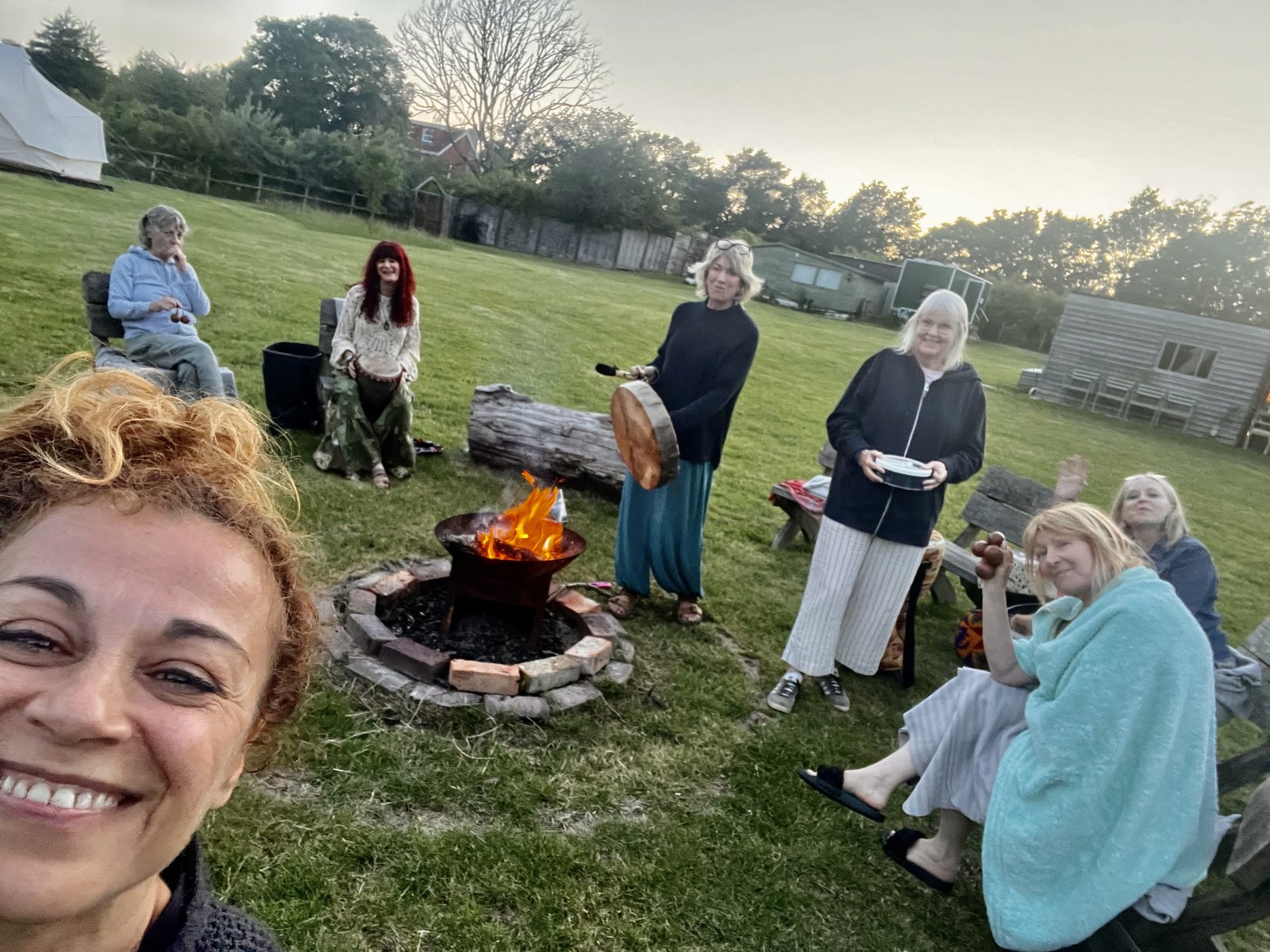 Women gathered around a fire pit with hand drums at dusk