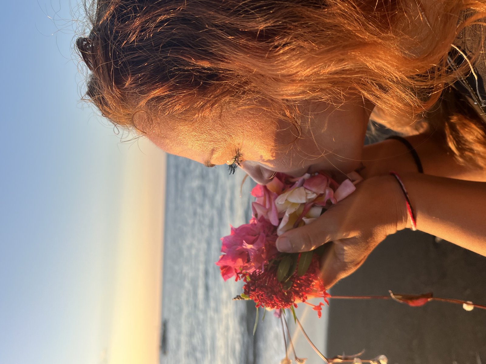 A close-up of a woman smelling a bouquet of flowers by the sea at golden hour