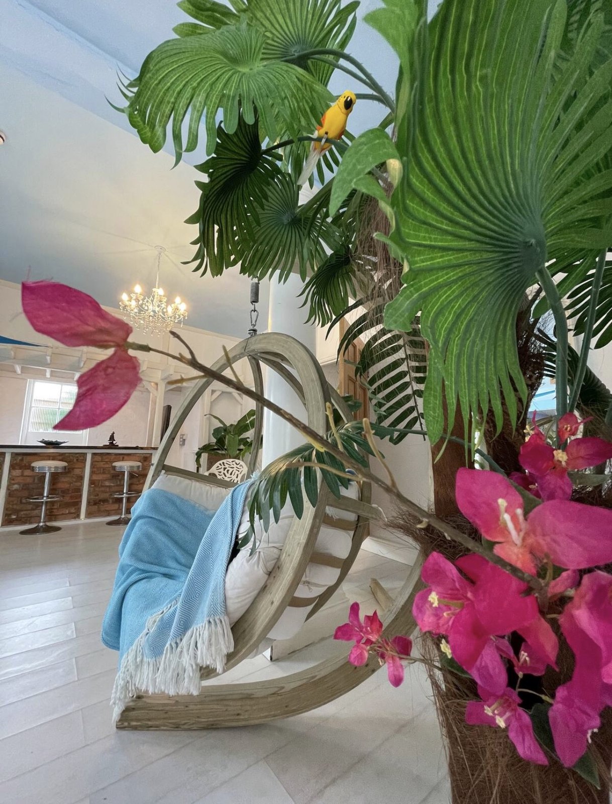 A hanging egg chair surrounded by tropical plants and pink flowers