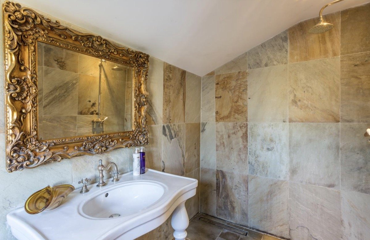 A marble bathroom with an ornate gold mirror