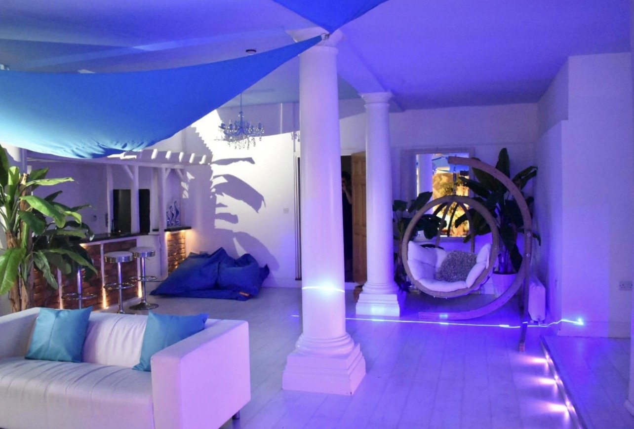 A purple-lit lounge at night with white columns and a hanging chair