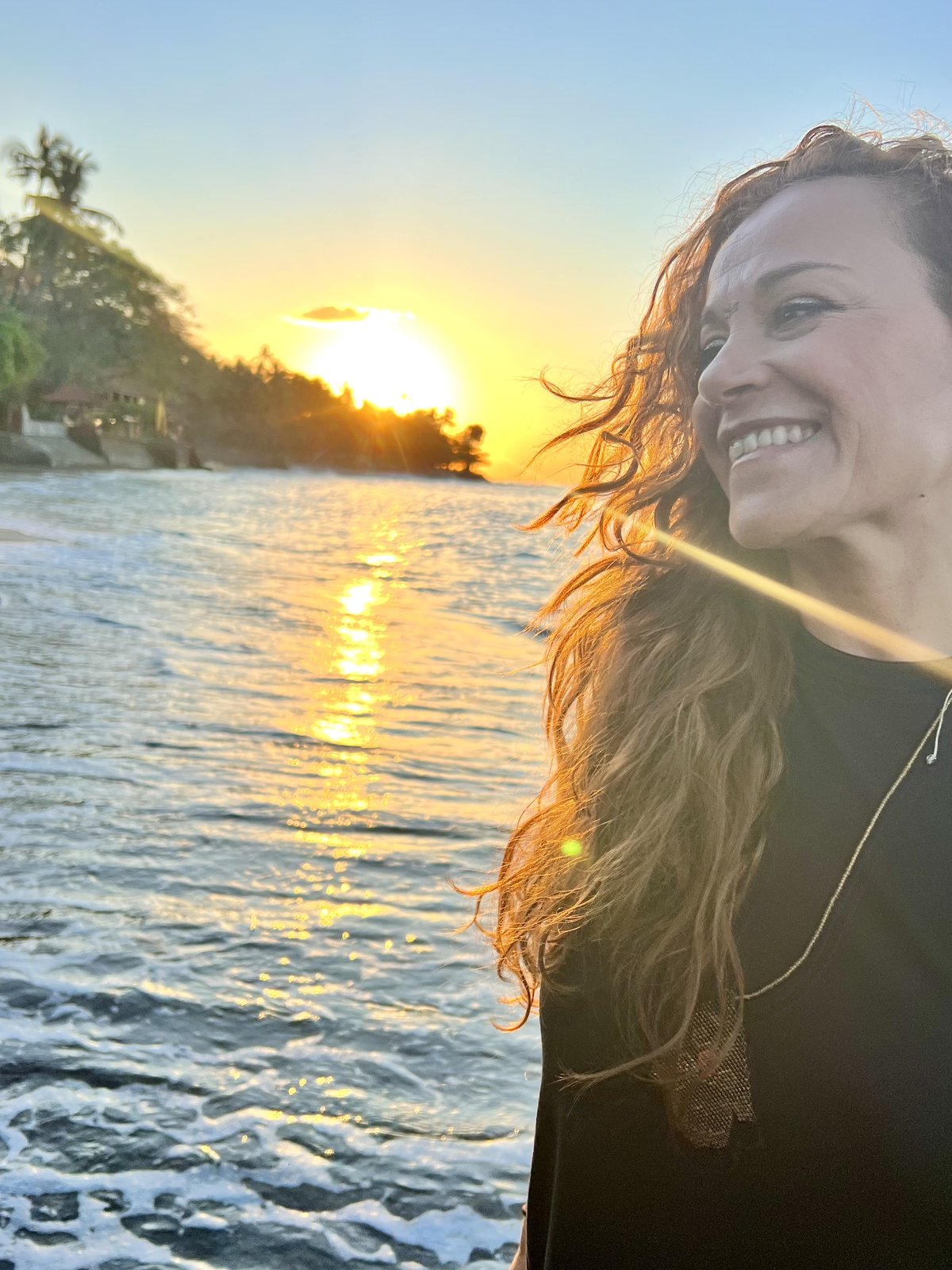 A woman smiling by the sea at sunset