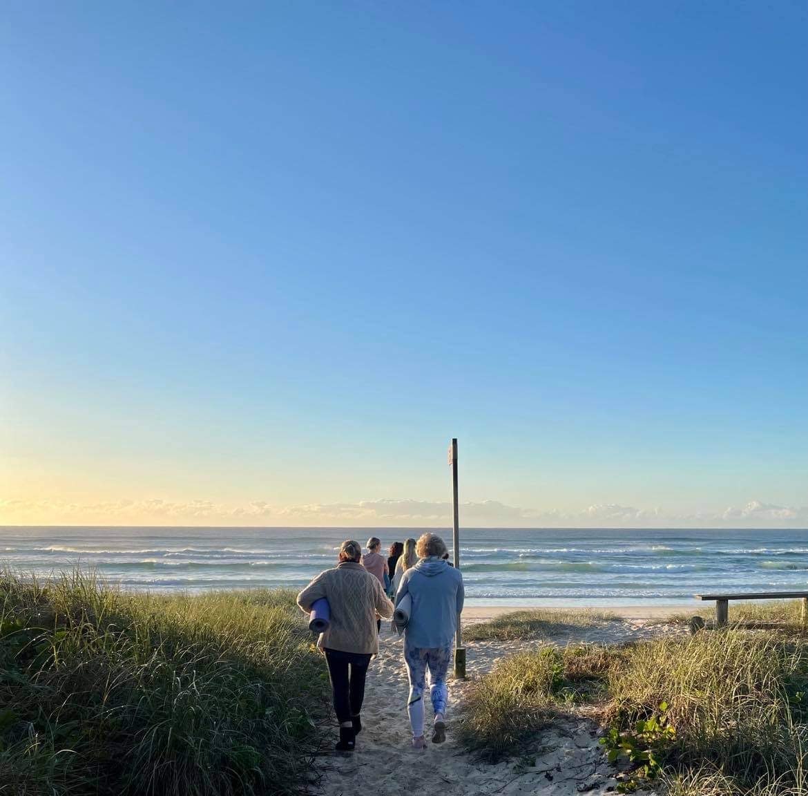 Guests walking to the beach with yoga mats at sunrise